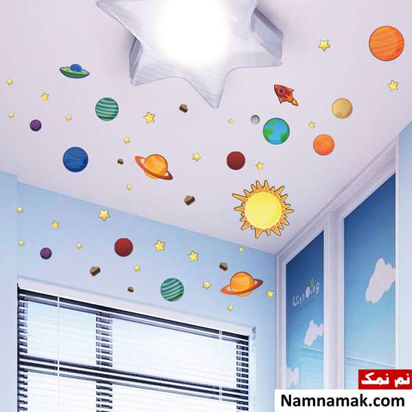 اتاق کودک با دیوارهای آبی و پرده کرکره ای که تزیین سقف آن با استیکرهای ماه و ستاره و سیاره های منظومه شمسی انجام شده است